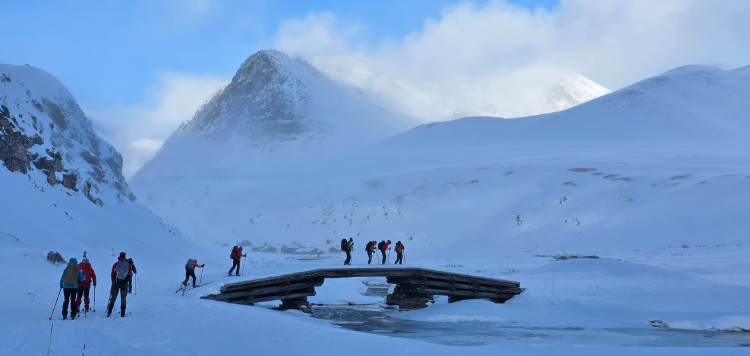 Een groep van 10 langlaufers die over een brug langlaufen