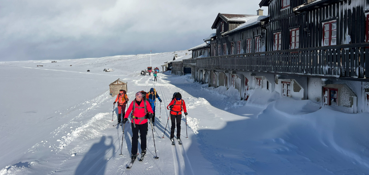 Vier langlaufers die langs de hut lopen waar ze overnacht zijn. 