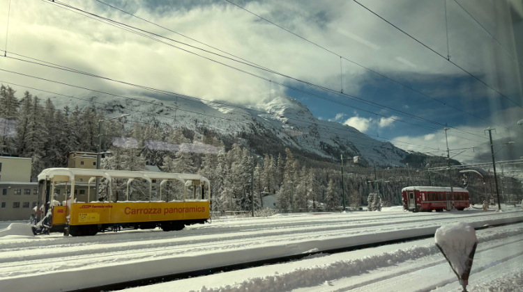 Foto vanuit een trein waarop je twee andere wagons ziet staan