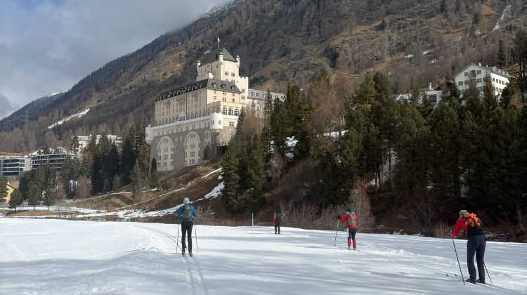 Vier langlaufers die over een loipe skien. Met een prachtig oud gebouw op de achtergrond