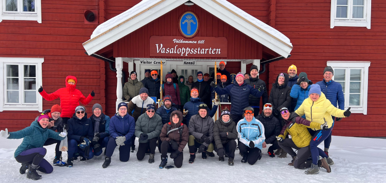 De volledige groep met deelnemers die mee gaan doen aan de Vasaloppet. Voor een rood huis waarop Vasaloppsstarten staat