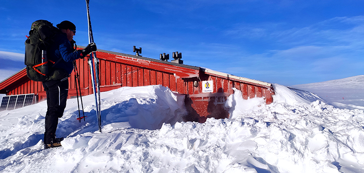 Skier staat met ski's in hand boven de ingesneeuwde hut